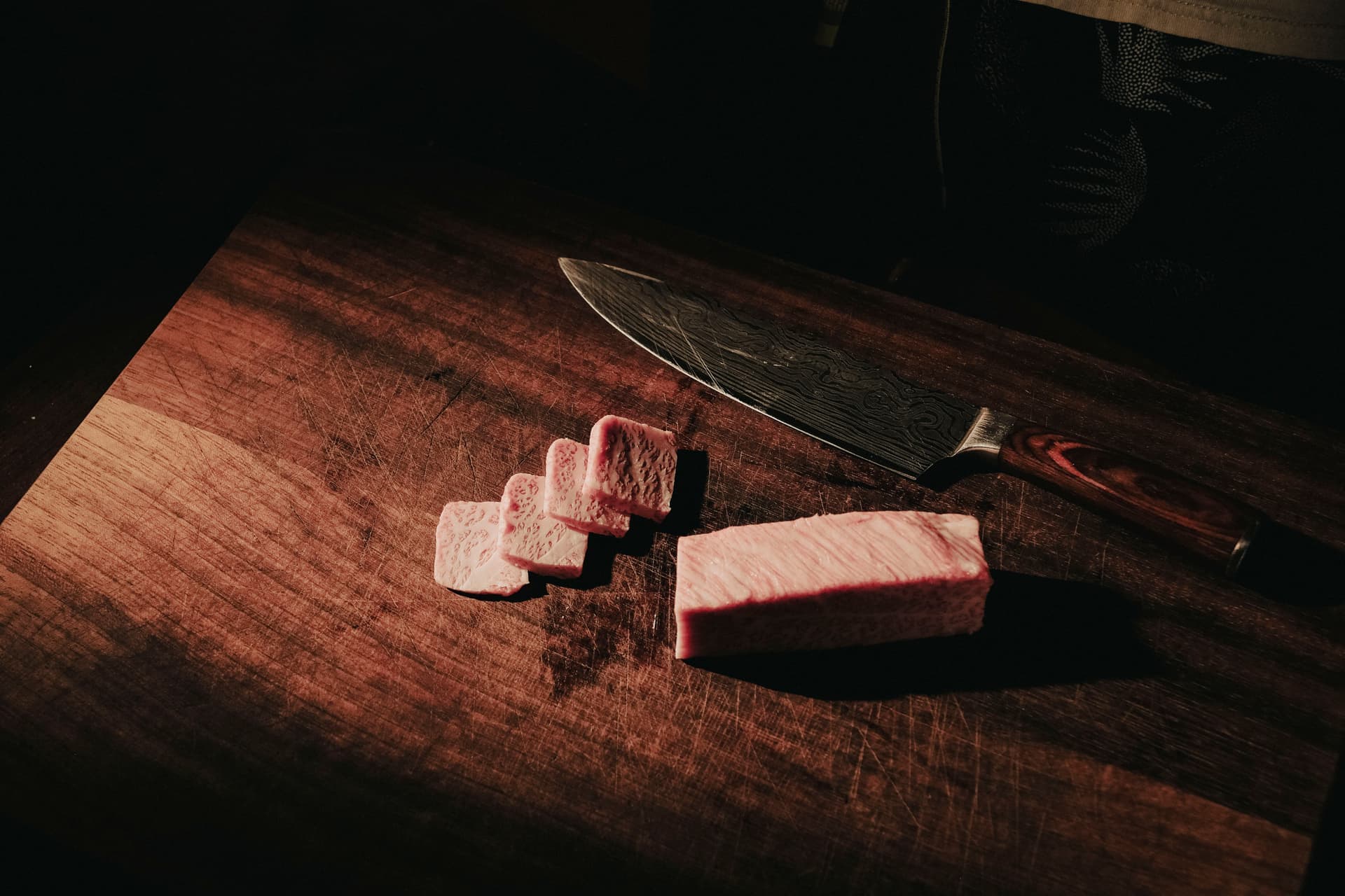 A Japanese chef's knife resting on a dark wooden board in soft light