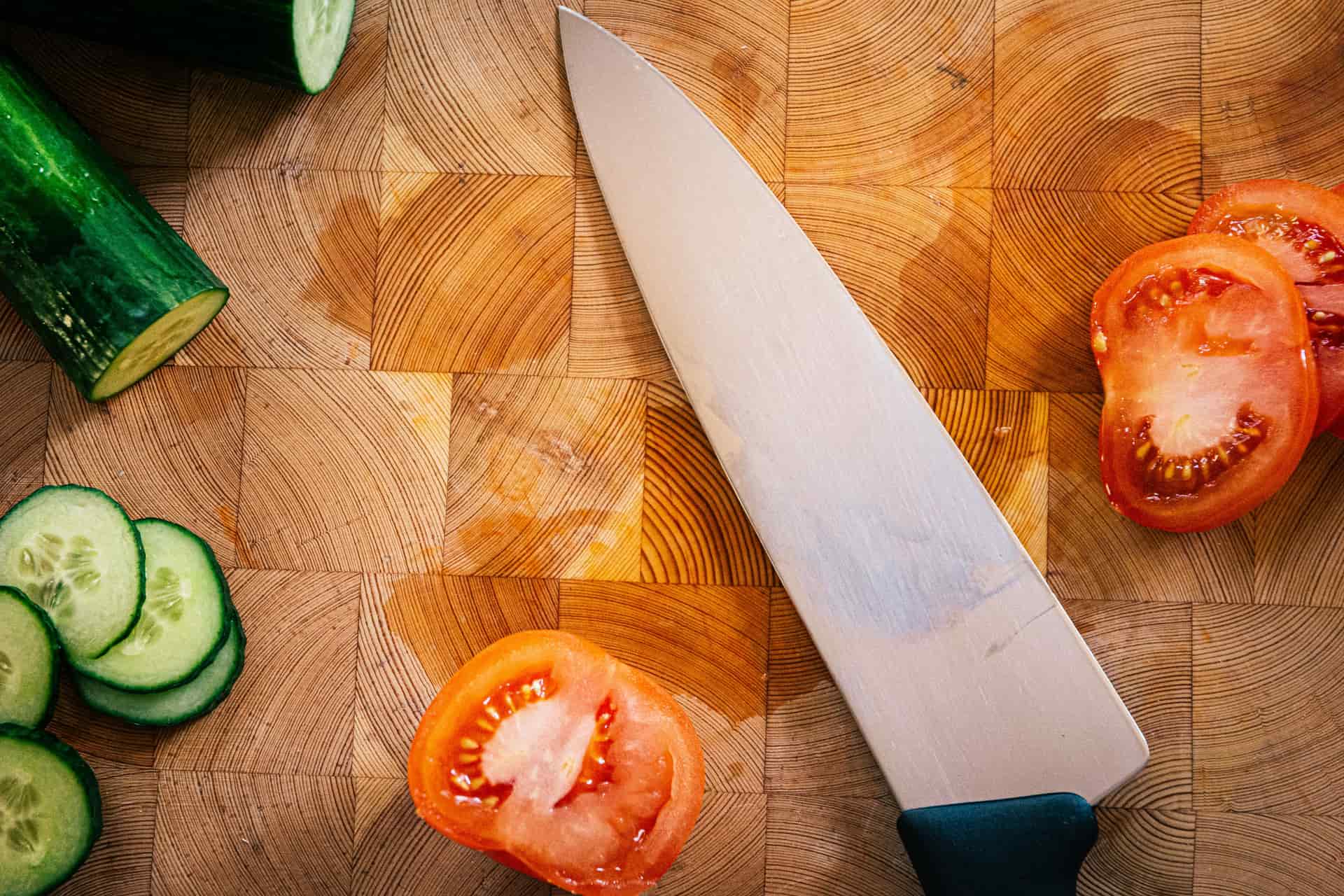 A chef's knife with fresh produce on a wooden board